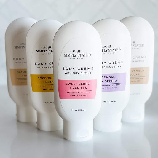 A collection of Simply Stated Body Creme 4oz squeeze bottles. Signature scents include Sweet Berry + Vanilla, Warm Vanilla + Sugar, Coconut Milk + Mango, Sea Salt + Orchid, and Oatmeal Milk + Honey for nourishing skincare.